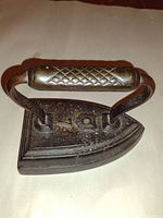 Photo showing top view of antique cast iron clothes iron with diamond pattern metal handle and cast iron base with markings