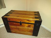 Front view of wooden travel trunk showing wood slats and metal lock in center.