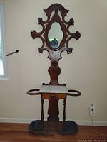 Full view of antique solid wood umbrella stand with marble top and oval mirror, showing drip dishes and umbrella holders on each side.