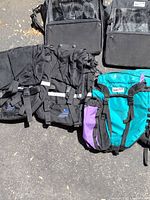 Photo of multiple black and teal/purple bike panniers laid on pavement, showing front and side views for condition and detail.