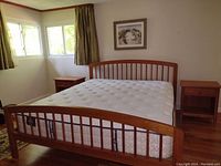 Full view of California King bed with mattress and two matching bedside tables in a bedroom setting showing light cherry wood and modern slatted design.