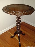 Carved round flip top table with dark stain finish, showing ornate carved border around table top and tripod pedestal base.