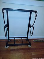 Front view of one black cast iron fish tank stand with decorative scrollwork on sides, rectangular base with slatted bottom and floor protective pads.