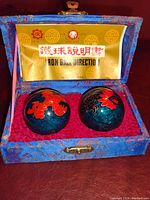 Inside view of open blue fabric box with pair of decorated blue and red metal stress relief balls and instruction leaflet