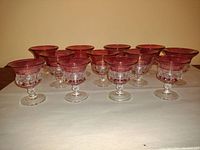 Front view of all twelve cranberry glass goblets showing two sizes and clear stems.