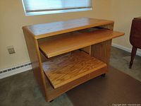 Front view of the solid wood desk on casters showing top surface, two pull-out shelves with wood grain finish, and caster wheels at base.