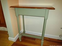 Front and side view of a small hallway table with cherry wood top and green painted legs connected by stretchers