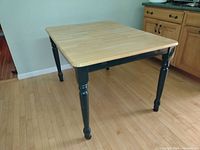 Photo showing the solid wood kitchen table with natural wood finish top and turned dark green painted legs, in a closed position.