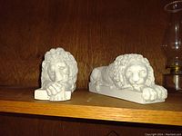 Front view of two white lion statues lying on shelf side by side.