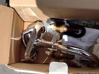 Photo of faucet components in box including spout, handles, valves, mounting hardware, and instructions.