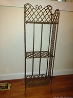Front view of the metal folding porch/plant stand showing the lattice shelf design and scroll detail on top.