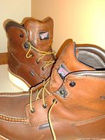Front view showing the brown leather Red Wing boots with brown laces and moc toe design, highlighting the altered thicker sole of the right boot.