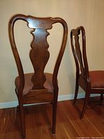 Photo showing the back of two chairs highlighting the carved splat and dark stained cherry wood frame.