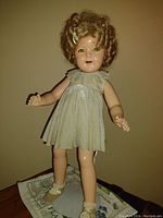 Full body image of the Shirley Temple doll standing, showing light polka dot dress and light shoes