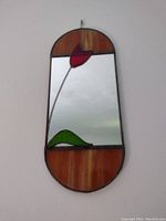 Front view of stained glass mirror showing red tulip design on mirror surface with amber toned stained glass framing.