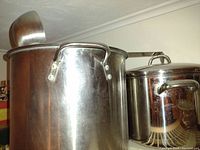 Two large stainless steel boiling pots with lids and handles on a shelf.