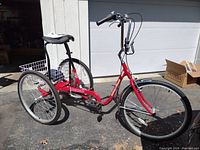 Front three-quarter view of red adult tricycle showing frame, front wheel and handlebars