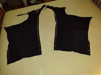 Photo of the two black leather chaps laid flat showing their design and snap closures on sides