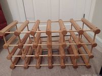 Photo of a light-colored wooden wine rack designed to hold wine bottles horizontally. The rack has a grid structure with horizontal wooden rods creating 28 spaces for wine storage.
