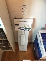 Photo showing the AncestryDNA kit and the Axis Gear motorized shade controller box against a wall and floor corner.