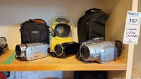 Three camcorders, eyepiece and cases on wooden shelf