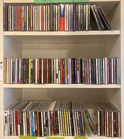 Three shelves filled with assorted music CDs in jewel cases