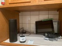 Photo showing tall black Amazon speaker SK705di, AWS smart device, Samsung digital picture frame and accessories on shelf.