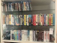 Three-shelf glass display showing mix of DVD, VHS and Blu-ray cases