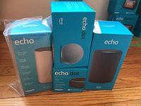 Photo showing four boxed smart speaker units, two Echo and two Echo Dot, in packaging with product branding and images.