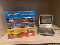 Stacked factory sealed Game Boy/Color game boxes next to Game Boy Advance SP on shelf