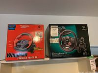 Photo showing two Logitech gaming steering wheels, one WingMan Formula Force GP and one Driving Force GT, both in unopened boxes.