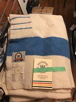 Folded cream wool blanket with wide blue stripe and attached pamphlet