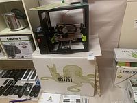 LulzBot Mini 3D printer placed on top of its original branded box featuring green octopus graphic