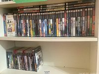 Top shelf packed with approximately 20 PlayStation 2 game cases, bottom shelf left showing PlayStation 3 cases