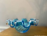 Close-up side view showing the fingered rim of the blue and clear glass bowl, highlighting the curvature and glass texture.