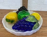 Top angled view of glass fruit and vegetable figurines in white bowl showing multiple colors and textures.