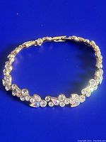 Full view of the gold tone Givenchy bracelet with clear and opalescent rhinestones laid flat on blue background