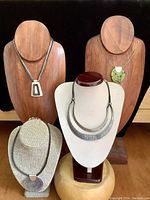 Six necklaces displayed on wooden and fabric necklace stands, showcasing variety in pendant shapes and materials.