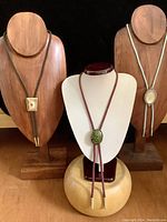 Three necklaces each with unique decorative pendants and suede or leather cords displayed on stands.