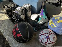 Three pairs of rollerblades, two basketballs, and one soccer ball arranged on the floor.