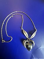 Full view of the necklace with leaf-shaped silver accents and heart-shaped onyx pendant on a blue surface