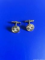 Pair of round gold plated sterling silver cufflinks with etched swirl design, shown on blue background.