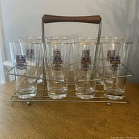 Front view of 8 vintage pilsner beer glasses with Quebec logo in metal stand with wooden handle on wooden surface