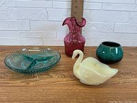 Photo showing four glassware items: blue divided dish, pink vase, white swan dish, and aqua vase with ruler for scale.