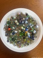 Top down view of a variety of glass marbles in a white bowl, displaying the range of colors and patterns.