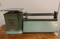 Side view of vintage green painted metal weigh scale with silver platform and sliding measurement bar.