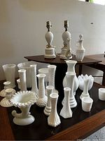 Overall view of milk glass collection including two hobnail lamps, vases and candle holders on wooden tables.
