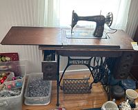 Full side view of Singer antique treadle sewing machine mounted in wooden cabinet with cast iron treadle base, drawers, and fold-out table wings