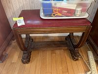 Front view of wooden framed bench seat with red vinyl cushion showing claw foot and curved leg supports.