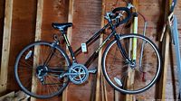 Full view of black women’s Schwinn bicycle with 22 inch wheels and drop handlebars leaning against wooden garage wall.